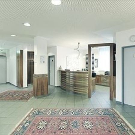 Ein moderner Empfangsbereich mit einem hölzernen Empfangstresen, Sitzgelegenheiten und dekorativen Teppichen, mit Kunstwerken an den Wänden.