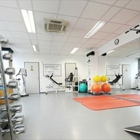 Heller und geräumiger Fitnessraum mit Hanteln, Fitnessgeräten, Stabilitätsbällen und verspiegelten Wänden für Trainingseinheiten.