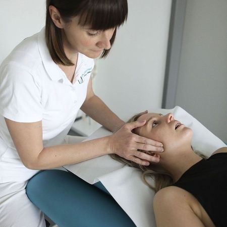 Eine medizinische Fachkraft behandelt einen Patienten, der auf einem Untersuchungstisch liegt, umgeben von Krankenblättern an der Wand.